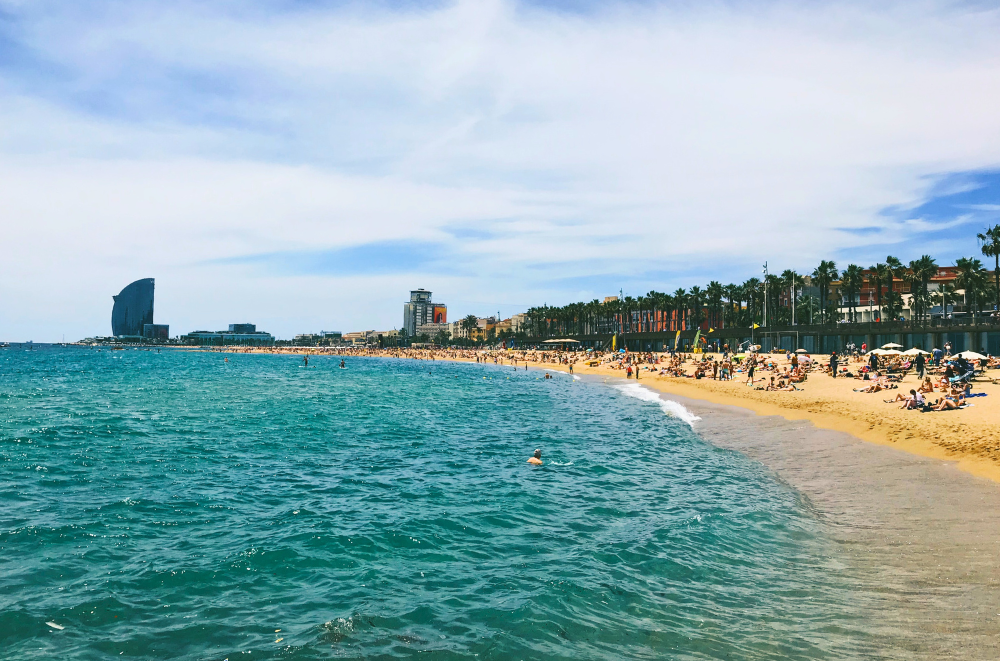 Barceloneta Beach in Barcelona with turquoise sea, golden sand, palm trees, and the W Hotel in the background