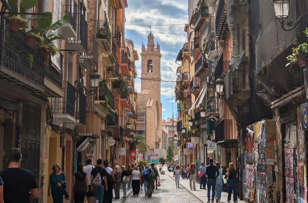 Bustling narrow street in Valencia old town with the historic El Micalet bell tower rising between traditional buildings and balconies